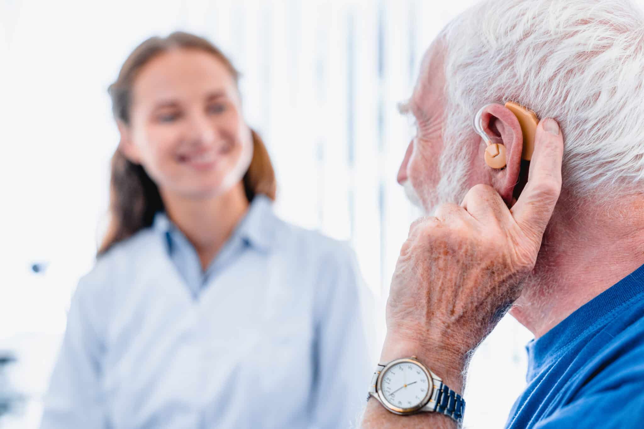 Older man with a hearing aid speaking to his audiologist/