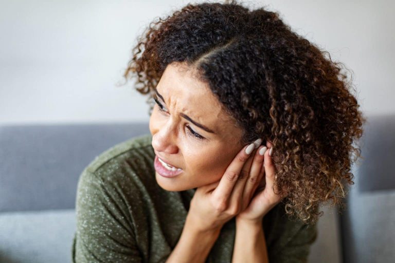 A woman experiencing severe tinnitus holds her hands to her ear.