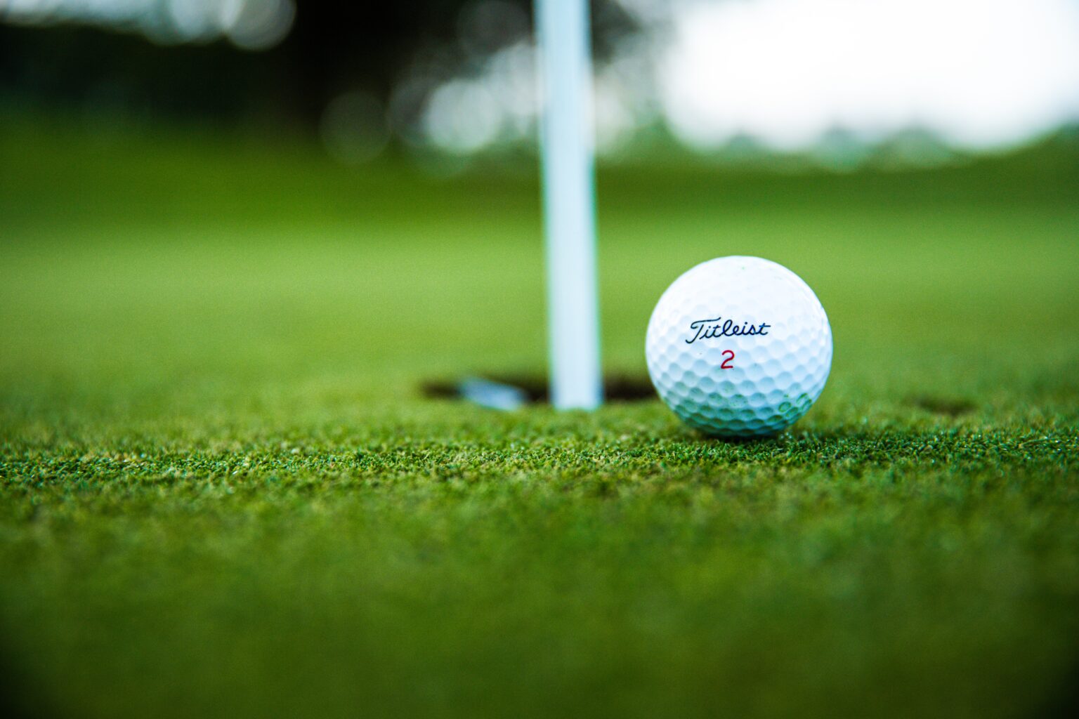 Golf ball sitting next to the hole on the green.