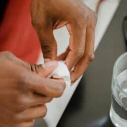 A pair of hands cleaning a hearing aid with a soft cloth.